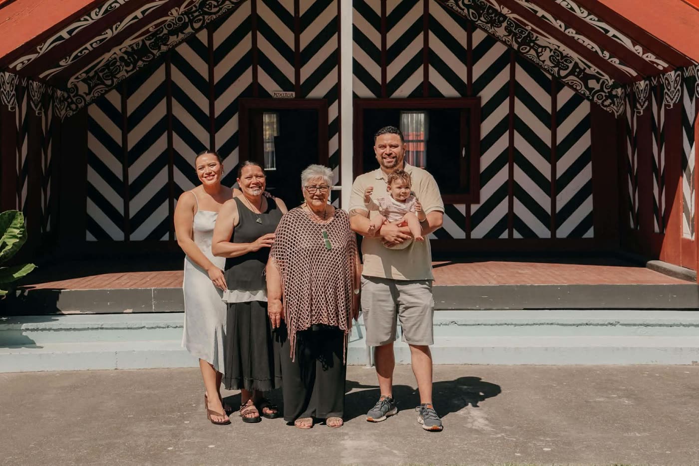 Four generations of whānau standing together in front of the wharenui