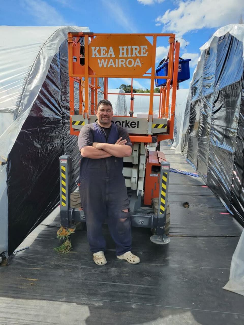 A whānau member at the scissor lift between greenhouse rows during the build